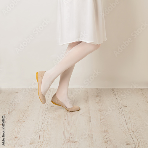 Female legs in white tights, skirt and ballet flats on a white background.
