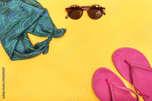 Top view of sunglasses, scarf and pink flip-flops on yellow, summer concept