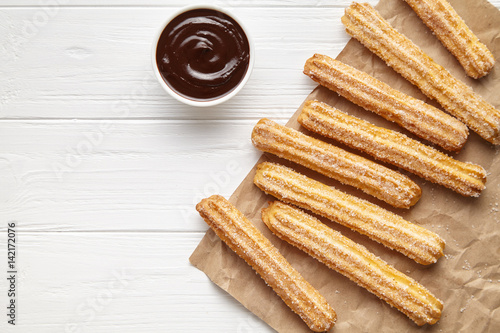 Churros traditional Spain street fast food baked sweet dough snack with chocolate, rustic decorative paper, white table background. Flat lay top view