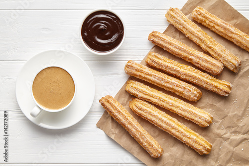 Churros traditional Spain street fast food baked sweet dough snack with chocolate and coffee, rustic decorative parchment paper, white table background. Flat lay top view