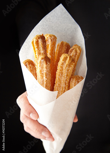 Churros traditional Spain or Mexican street fast food baked sweet dough snack in hand cone of parchment paper