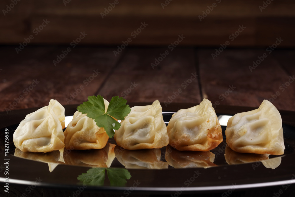 A plate of Japanese gyoza dumplings sitting on a rustic wooden table. A plate of Japanese gyoza dumplings sitting on a rustic wooden table.