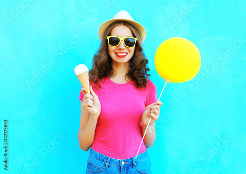 Fashion happy smiling woman with yellow air balloon and ice cream cone wearing straw hat and pink t-shirt over colorful blue background