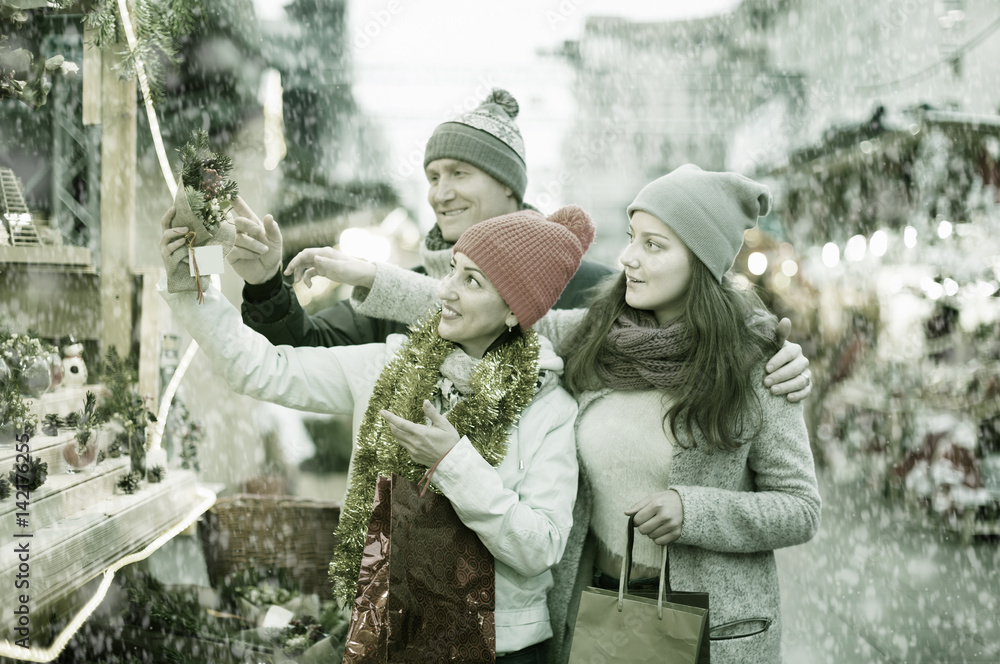 attentive family couple with teen girl choosing Christmas decoration