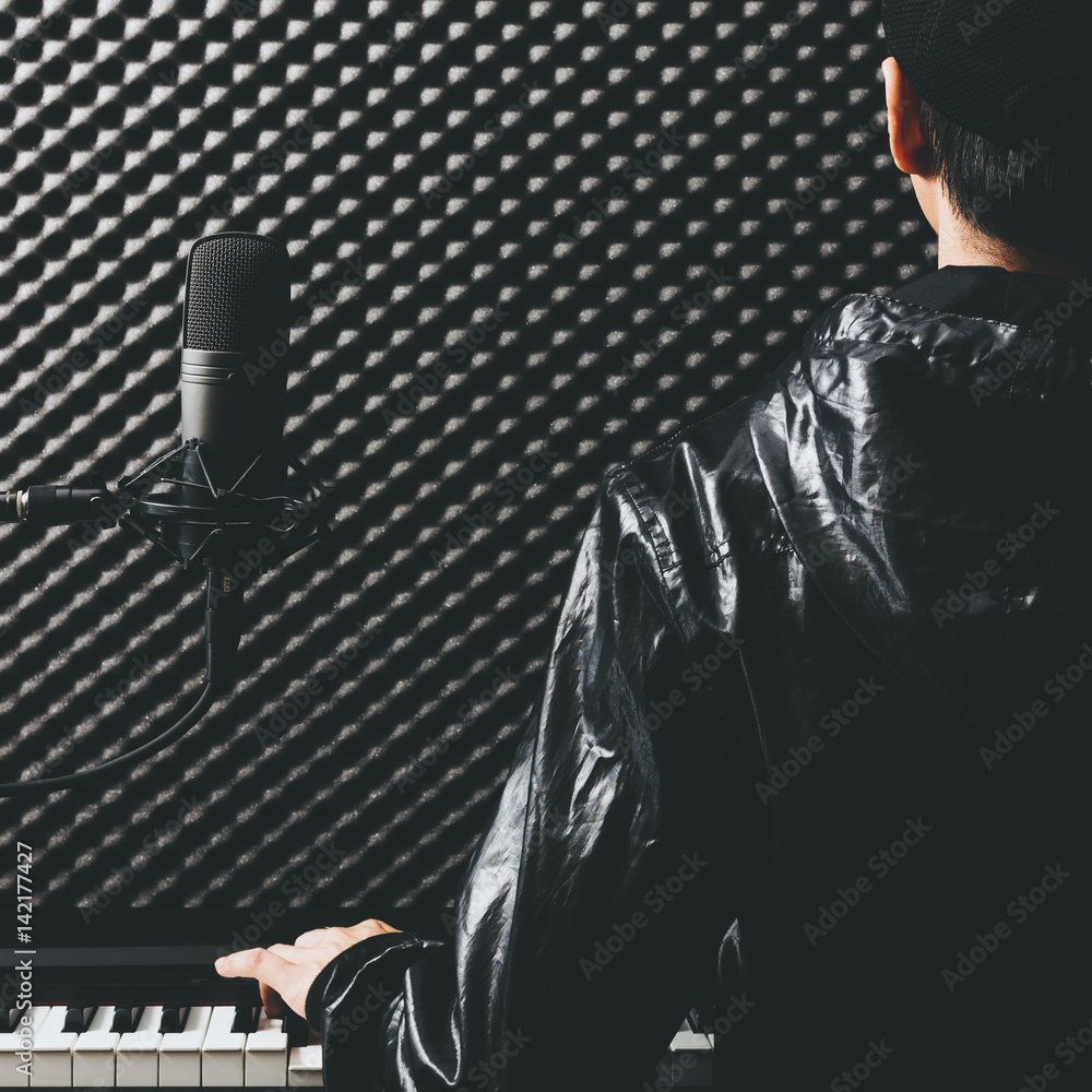 back of male asian musician playing piano with microphone in recording studio