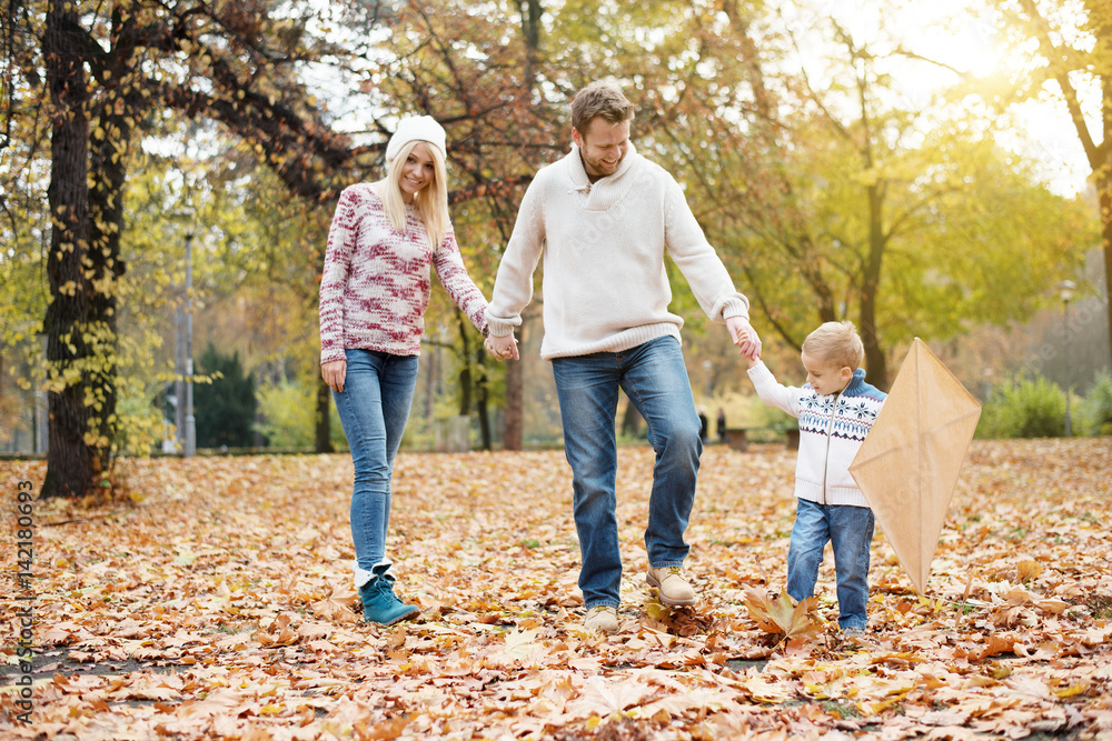 Happy family walking in park through the fallen leafs, they are holding hands Happy family walking in park through the fallen leafs, they are holding hands