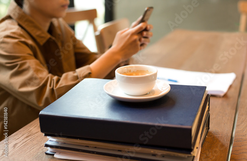 Selected focus coffee cup on top of folders with student looking cell phone looking cell phone