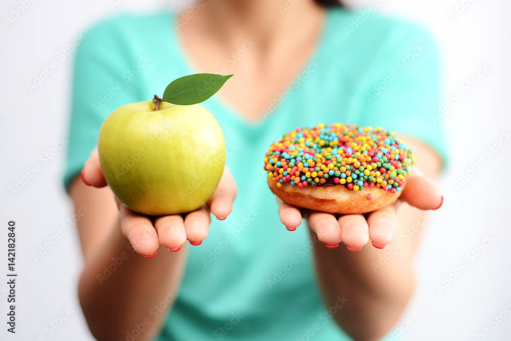 Plakat Trudno wybrać koncepcję zdrowej żywności, z kobiecą ręką trzymającą zielone jabłko i pączkiem z bombą kaloryczną