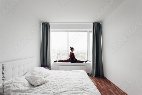 Pretty young woman doing yoga exercise at home on a window