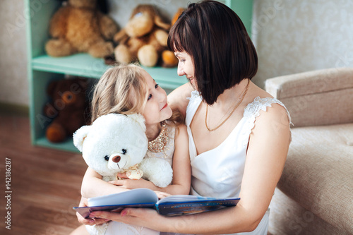 Happy mother and daughter are sitting in the room reading a book