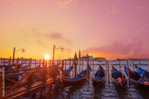 Traditional Italian gondolas moored to the poles in Europe Venice near the city center and Saint Mark square with a background view of the church of San Giorgio Maggiore at sunrise time © nevodka.com