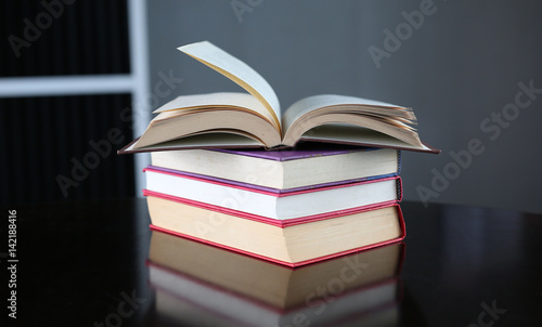 Open book with stack of hardcover books on wooden table.