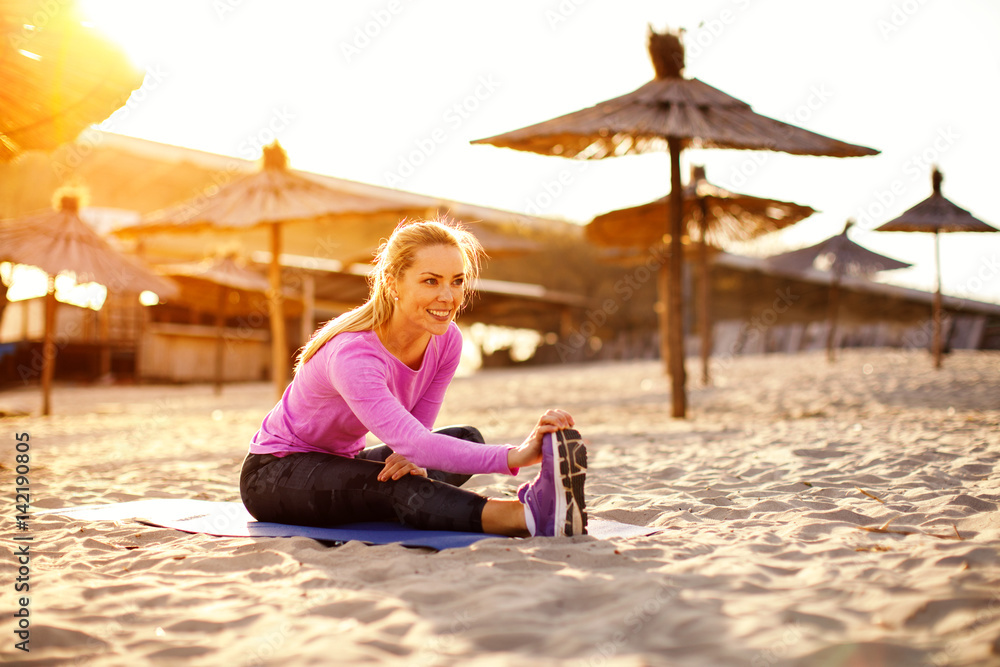Beautiful blonde woman stretching legs on beach at sunset