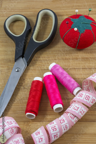 Sewing tools with red pincushion are on the wooden background