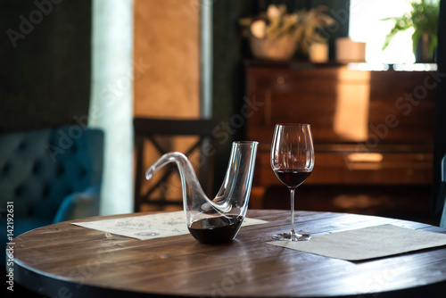 Decanter with red wine and glass on wooden table in interior. Free space for text. Still life photo