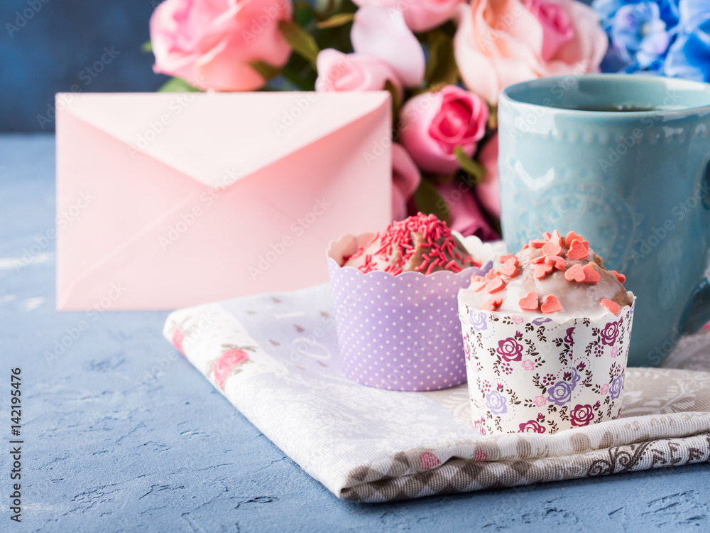 Mother's day Valentine concept muffins with hearts sprinkles and cup of tea on napkin. Flowers Mother's day Valentine concept muffins with hearts sprinkles and cup of tea on napkin. Flowers