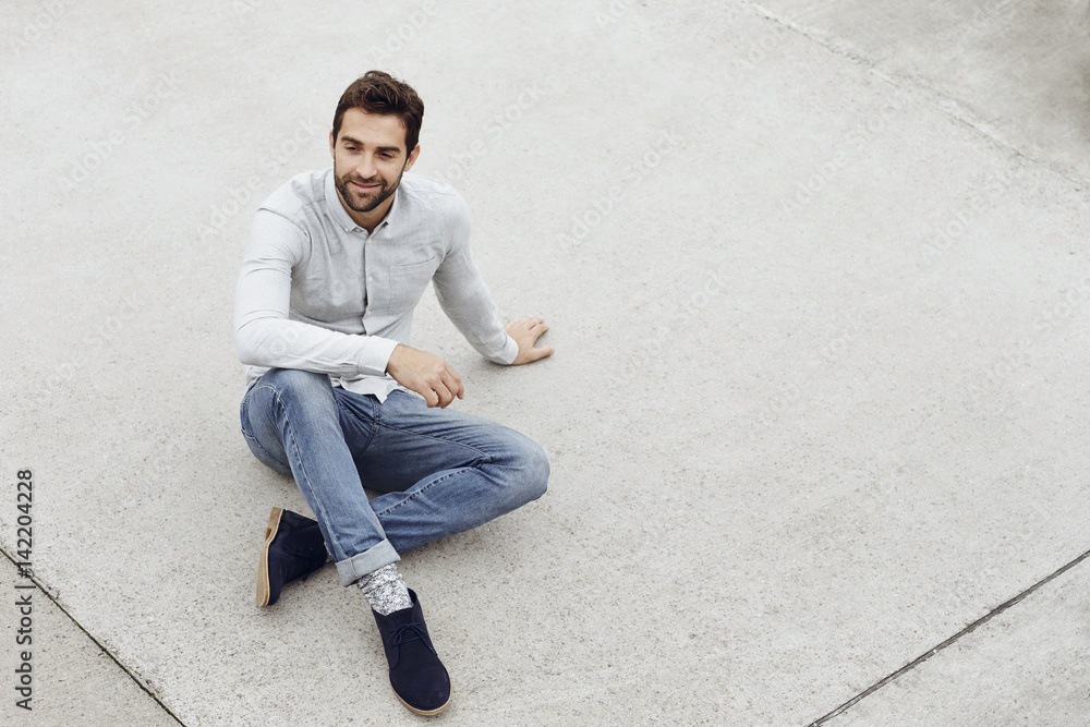 Dude in jeans sitting on pavement, smiling Dude in jeans sitting on pavement, smiling