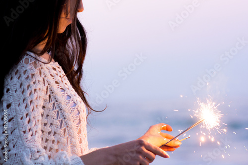 Woman having fun with sparklers near the sea at the evening