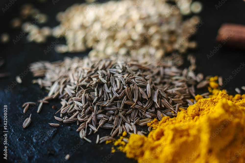 Cumin seeds surrounded by spices over black surface.