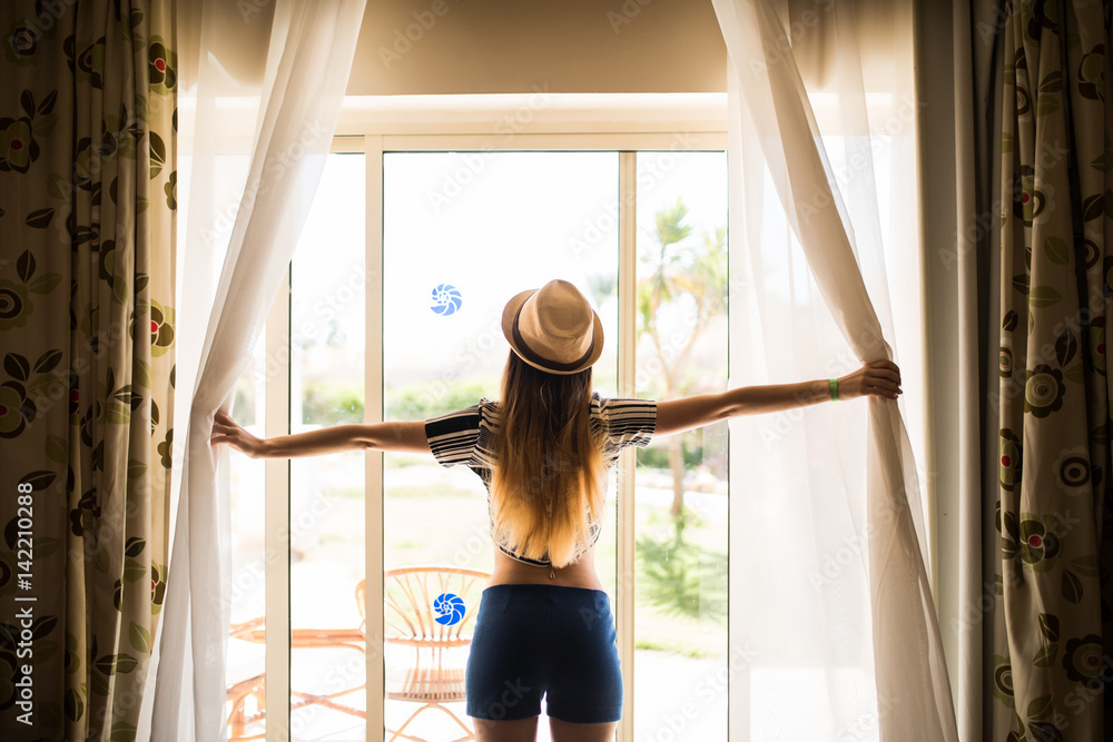 girl in hat opens the curtains, Summer morning in hotel room girl in hat opens the curtains, Summer morning in hotel room