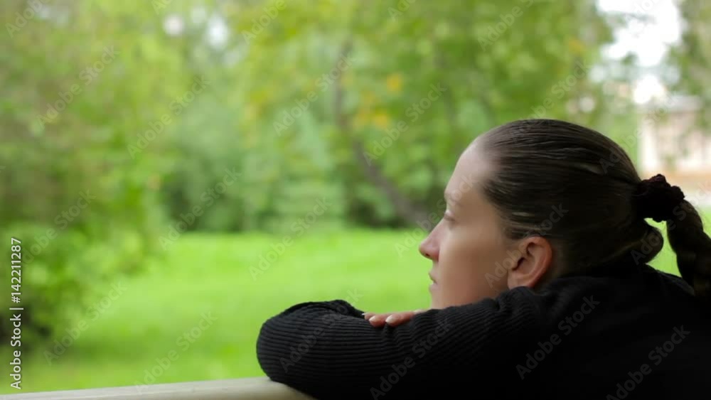 Pensive thoughtful girl meditates on the background of green trees and grass in summer day at park. Beautiful young woman with braid in a black dress thinks. Contemplates greenery of nature. Close-up Pensive thoughtful girl meditates on the background of green trees and grass in summer day at park. Beautiful young woman with braid in a black dress thinks. Contemplates greenery of nature. Close-up