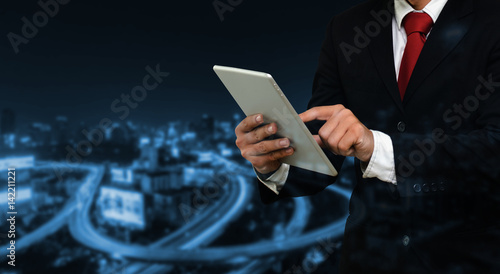 smart businessman in suit using his tablet, business and technology concept on blurred night city background,copy space, color tone effect.