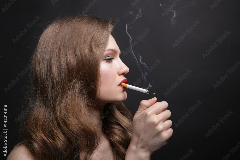 Fototapeta premium Portrait of beautiful woman with cigarette on black background