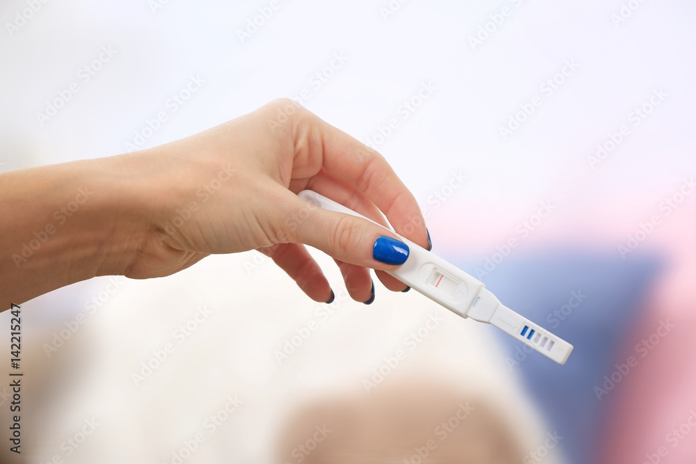 Pregnancy test in hand on blurred background of living room Pregnancy test in hand on blurred background of living room