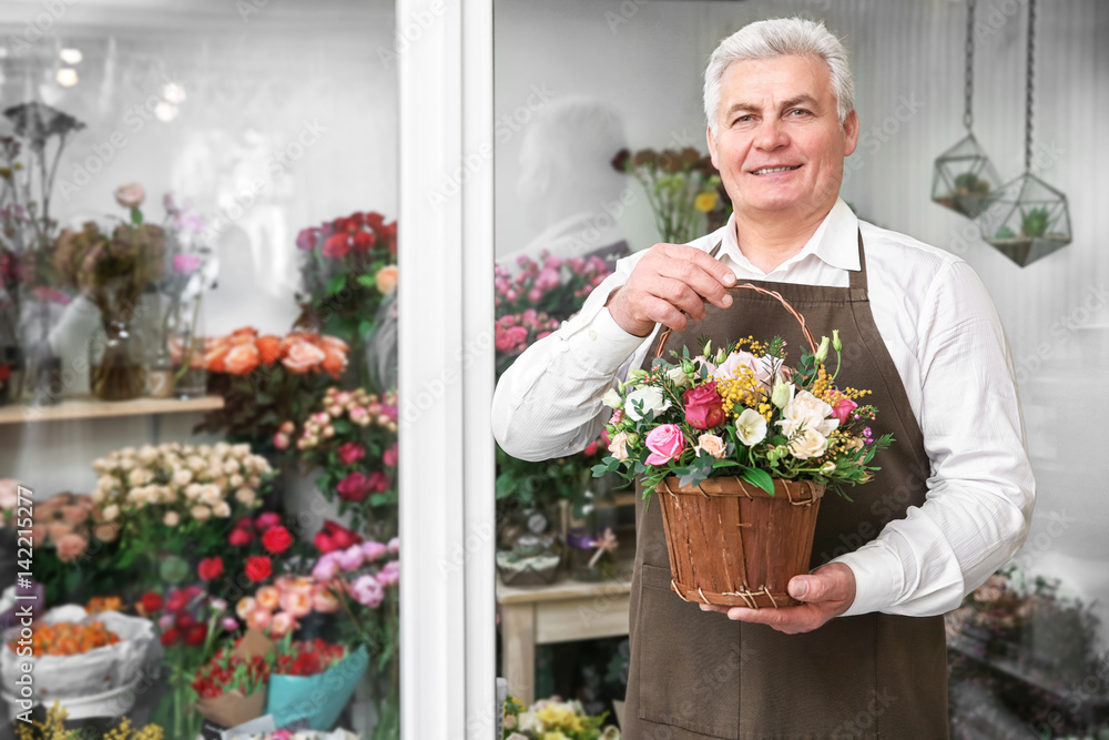 Male florist holding basket with flowers in flower shop