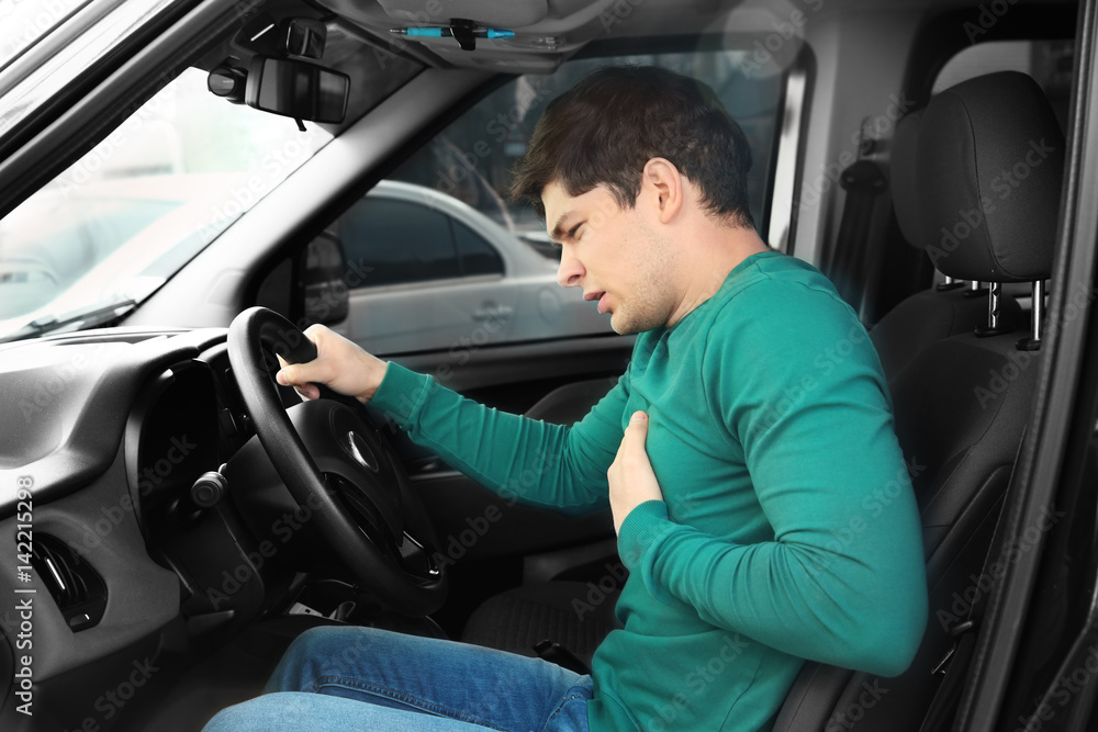 Heart attack concept. Young man suffering from chest pain sitting in car Heart attack concept. Young man suffering from chest pain sitting in car