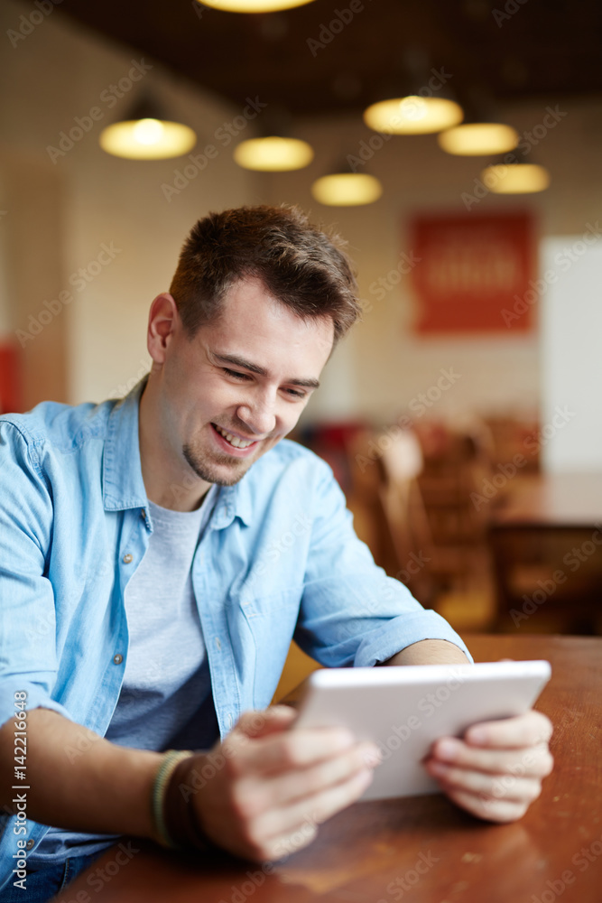 Portrait of modern young man playing video game using portable digital tablet in cafe and smiling joyfully Portrait of modern young man playing video game using portable digital tablet in cafe and smiling joyfully