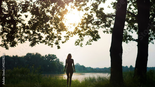 Fototapeta Naklejka Na Ścianę i Meble -  Beautiful Young Woman near forest lake at sunrise or dusk, silhouette