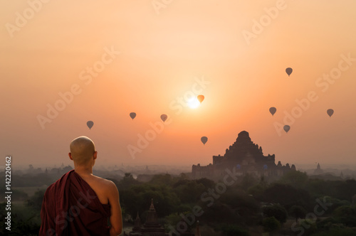 Monk looking at hot air balloons at sunrise at Bagan temple in Burma, Myanmar