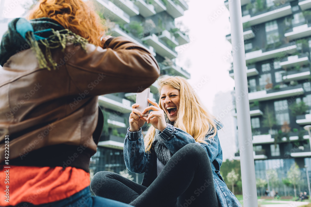 Two young women using smart phone outdoor taking photos - technology, social network, communication concept Two young women using smart phone outdoor taking photos - technology, social network, communication concept