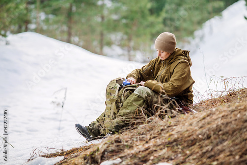 Hunter girl sitting with backpack and drinking water outdoor snow forest in background.