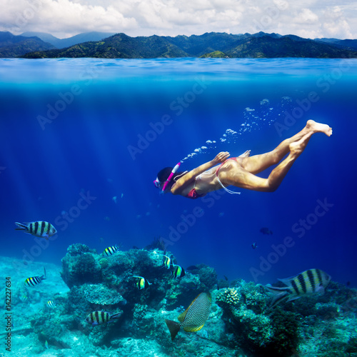 Underwater shoot of a young woman snorkeling in a tropical sea and coast mountain splitted by waterline