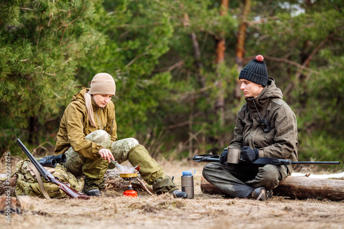 .Two hunters are eating together in the forest. Bushcraft, hunting and people concept