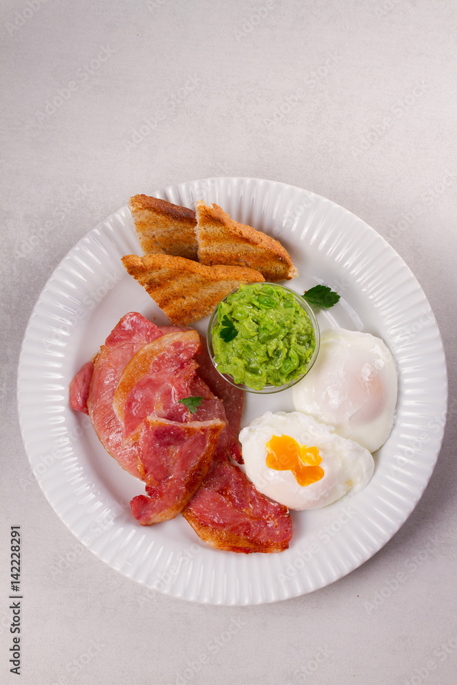 Bacon, poached eggs, mashed peas and toasts on white plate. Grilled rashers and eggs Bacon, poached eggs, mashed peas and toasts on white plate. Grilled rashers and eggs
