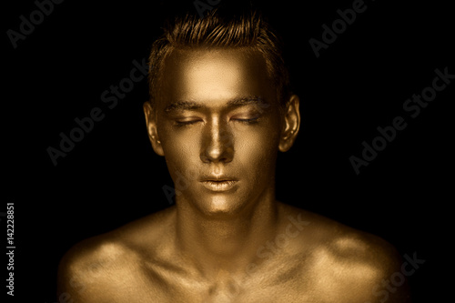 A handsome man of athletic build, completely covered in gold paint.Studio photos