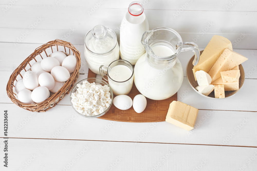 Top view of a set of products consisting of milk, butter, curd, cheese and eggs on white wooden table Top view of a set of products consisting of milk, butter, curd, cheese and eggs on white wooden table