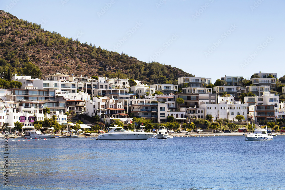 View of yachts and Icmeler area of Bodrum city. White summer houses reflects region's architectture style. It's a calm, hot summer day.