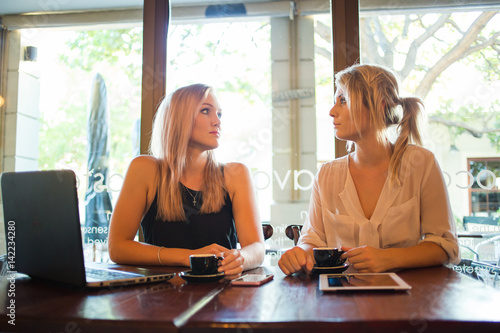 two young blond female business women having a business meeting in a coffee shop over a cup of espresso