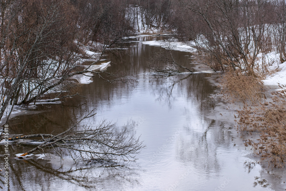 A dull gray landscape in early spring begins to melt snow and ice, a reflection in the river. A dull gray landscape in early spring begins to melt snow and ice, a reflection in the river.