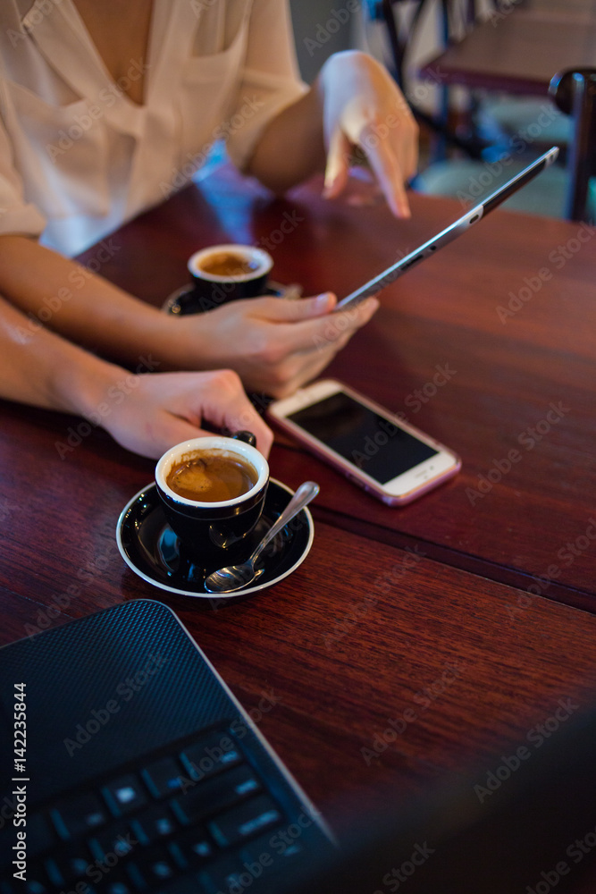 Close up of two female model's hands using smart devices while having coffee in a coffee shop as part of their business meeting