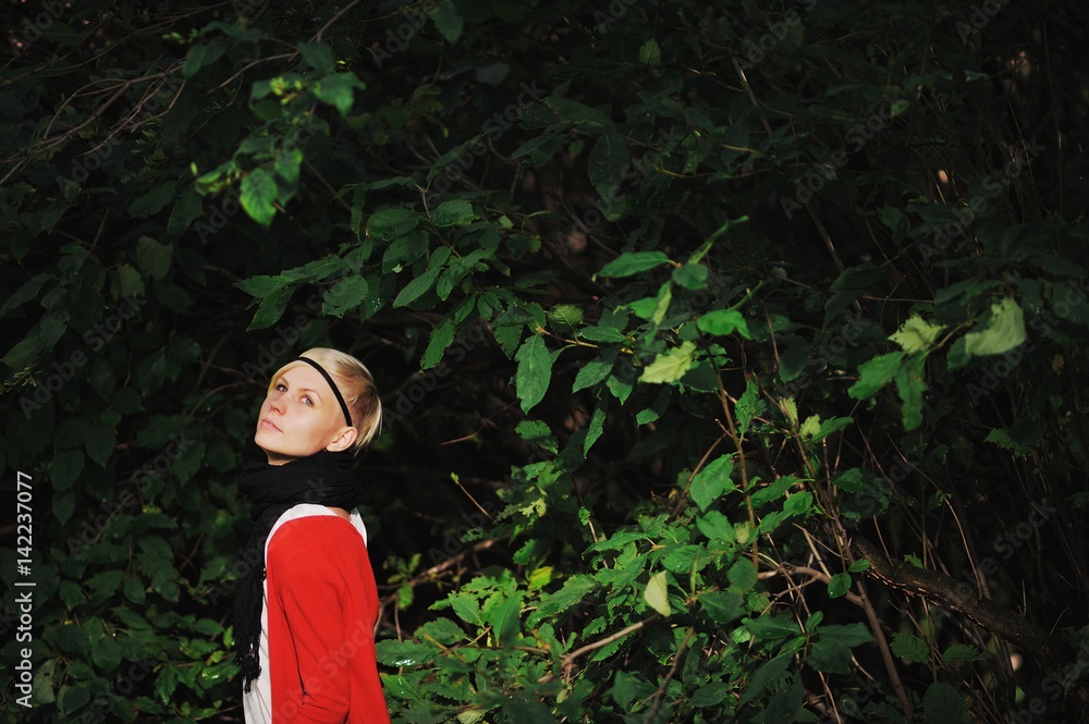 beautiful blonde girl in white shirt and red cardigan among green leaves enjoys in the sunlight beautiful blonde girl in white shirt and red cardigan among green leaves enjoys in the sunlight
