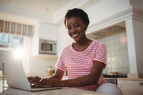 Portrait of smiling woman using laptop in kitchen Free Download Portrait of smiling woman using laptop in kitchen - GFXLoad