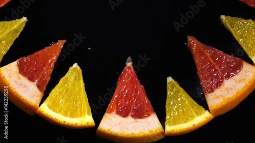 Excellent top view of fresh orange and red grape-fruit sector slices, put in ring on black dish, rotating clockwise with up center. Flat lay of dessert on dark background with amazing texture in 4k.