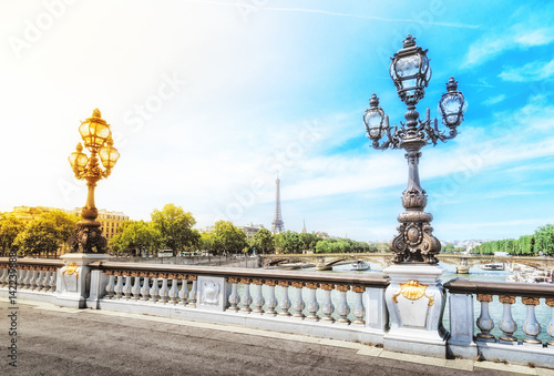 Alexandre III bridge over the river Seine with the Eiffel tower in the background in Paris, France. Decorative lamp at foreground. Dramatic sky at background with opposite colors - yellow and blue.