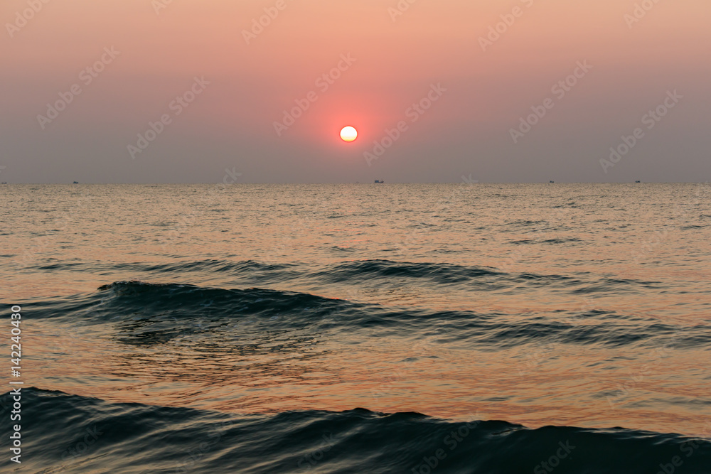 Beach sunset is a golden sunset sky with a wave rolling to shore as the sun sets over the ocean horizon