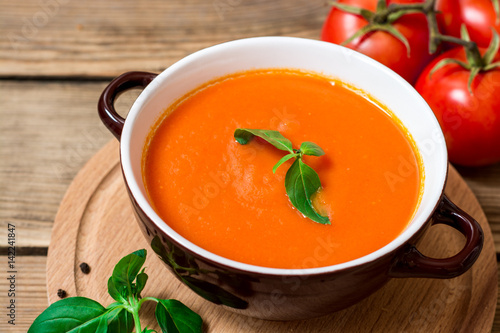 Tomato soup in ceramic bowl on wooden background.